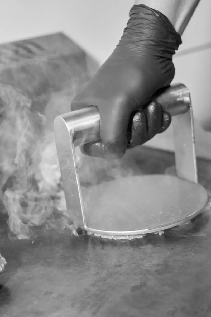 Mano con guante presionando la prensa de acero sobre la plancha caliente, con vapor